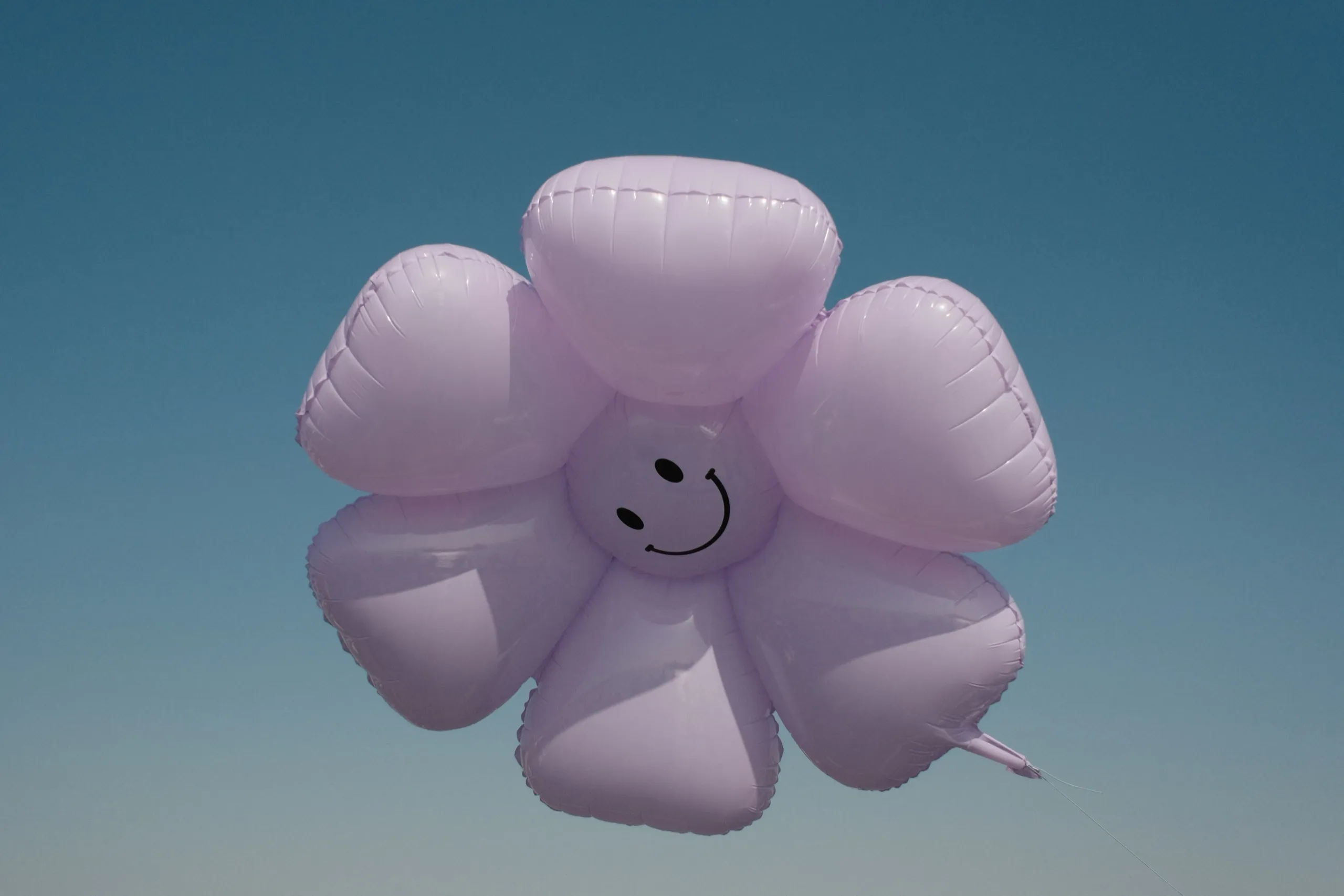 A lilac flower-shaped balloon with a smiley face against a clear blue sky