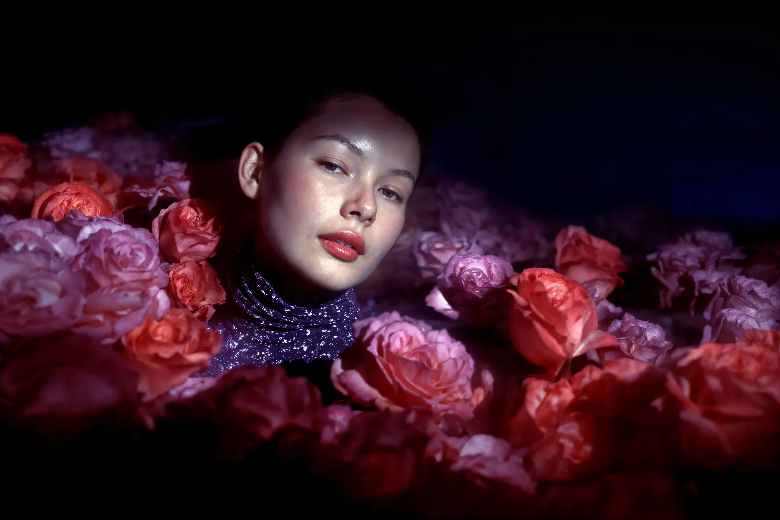 AI-generated portrait of a woman's head and sequined collar rising out of a bed of red and pink roses in the dark