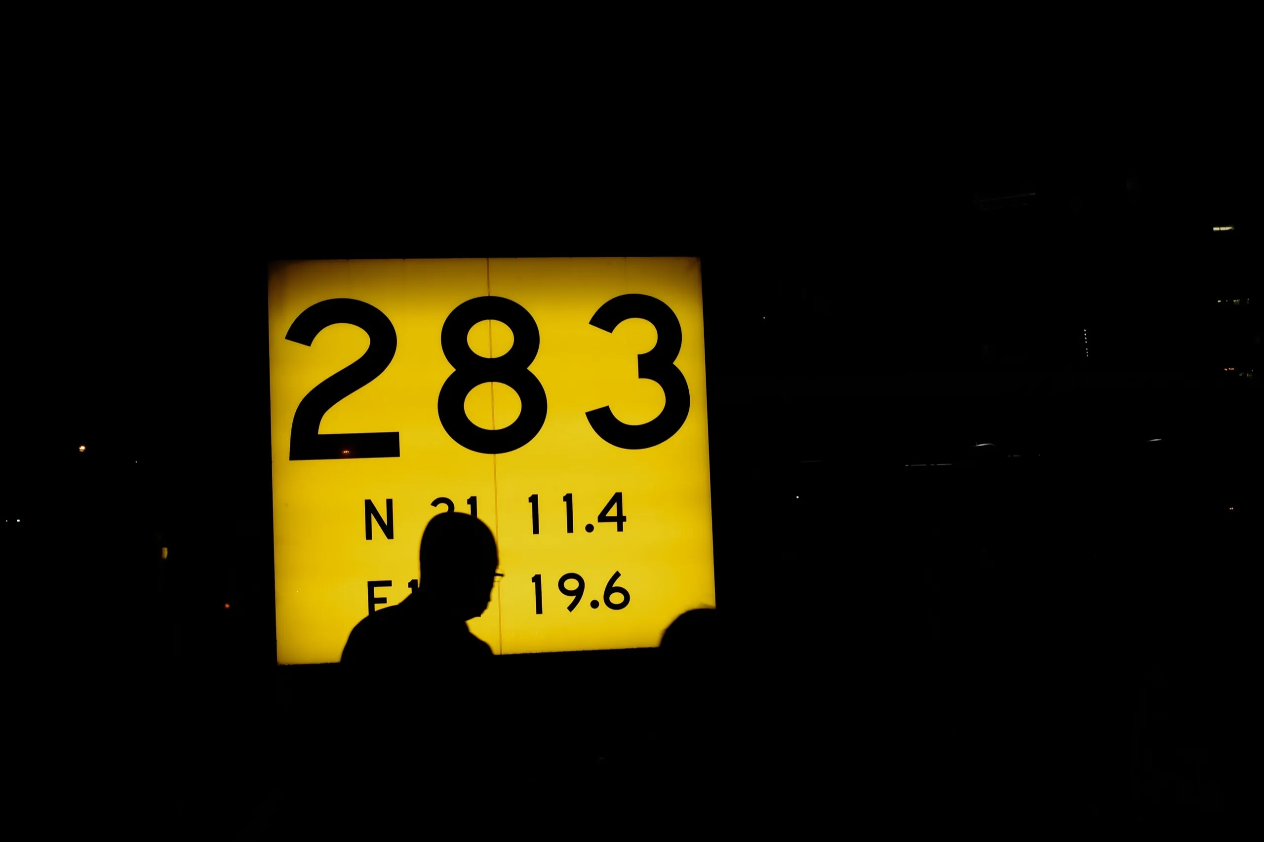 A silhouette passing a glowing yellow sign with the number 283 in the dark