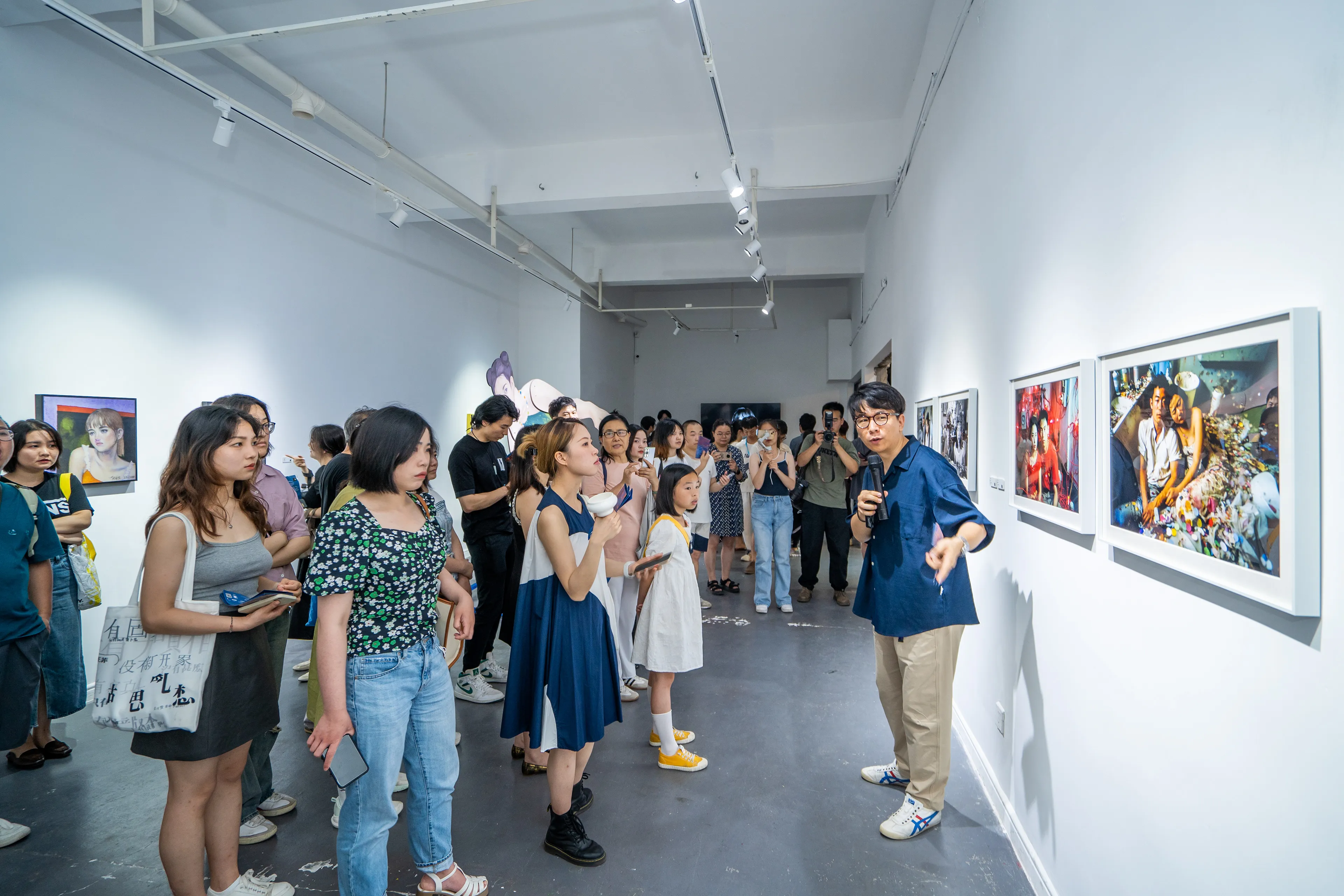 Me with a microphone at the opening of the group show Cabinet of Curiosities at Forward Art Gallery in Changsha, talking visitors through the framed prints of my AI-generated portrait series Lovers.