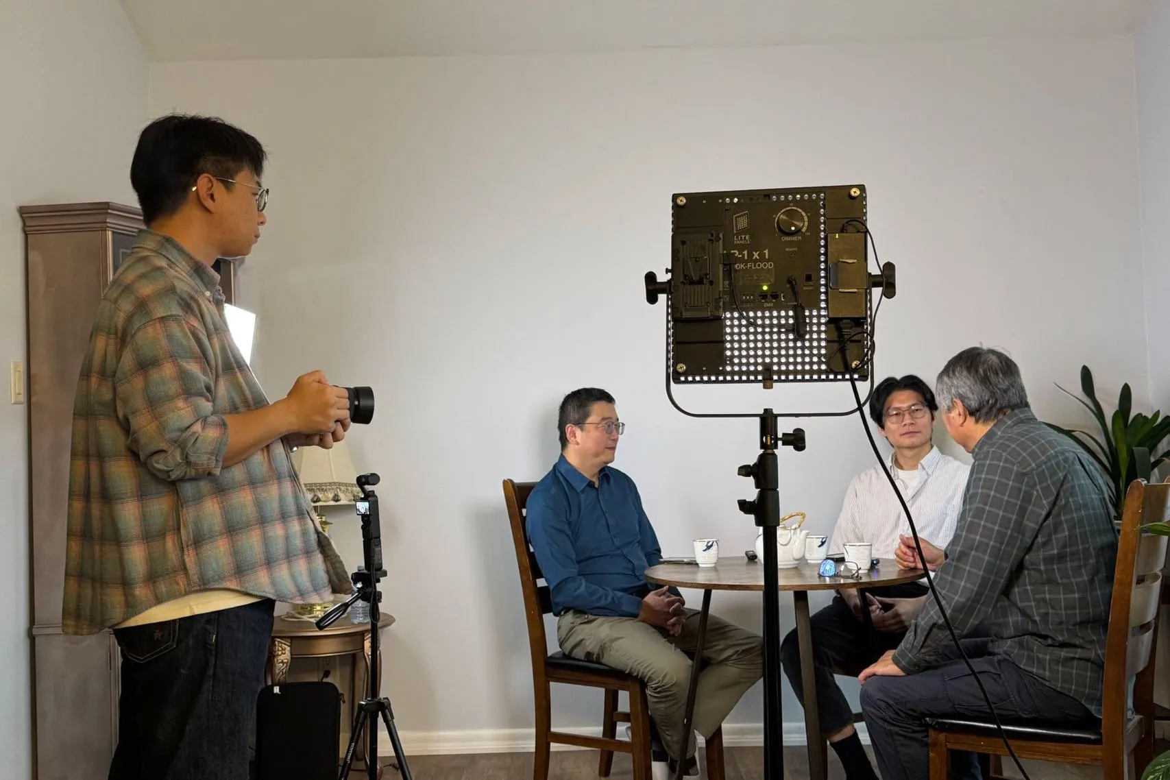Me with a camera at an interview shoot for my friend Frank Yang: three men talk at a small table under an LED panel.